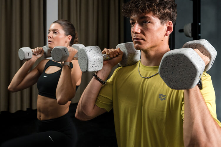 Ragazza e ragazzo che si allenano con i pesi in palestra e sono vestiti con apparel Arena