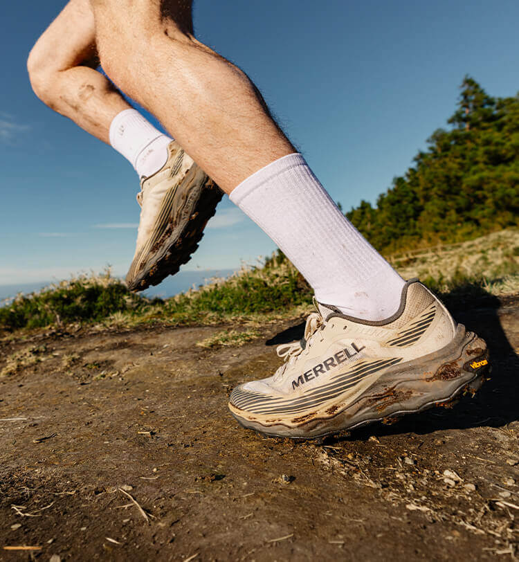 Ragazzo che fa trail running in alta montagna con scarpe Merrell